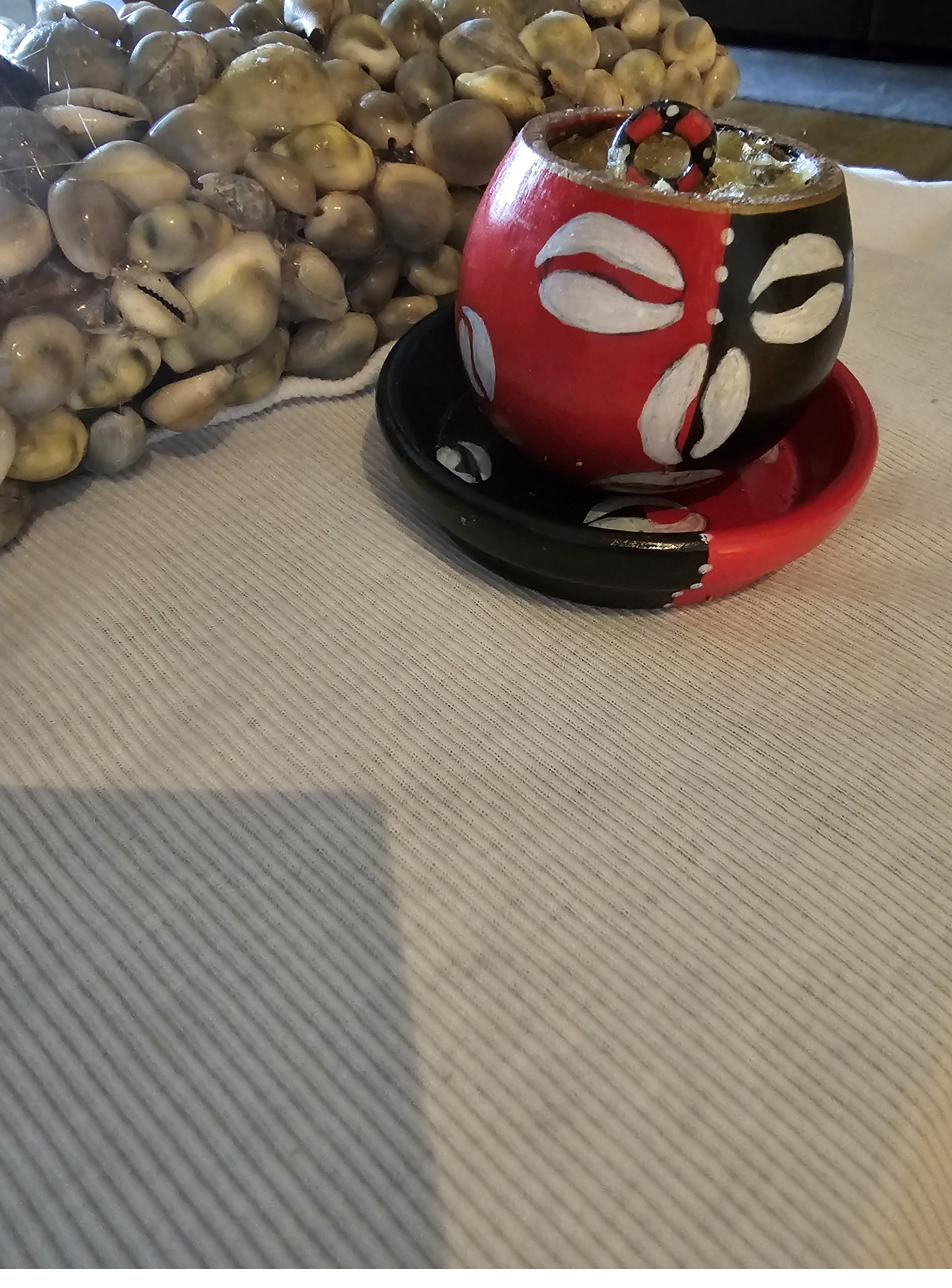 Ritual object, London: a red and black painted vessel for Eshu alongside a bag of shells on a woven surface